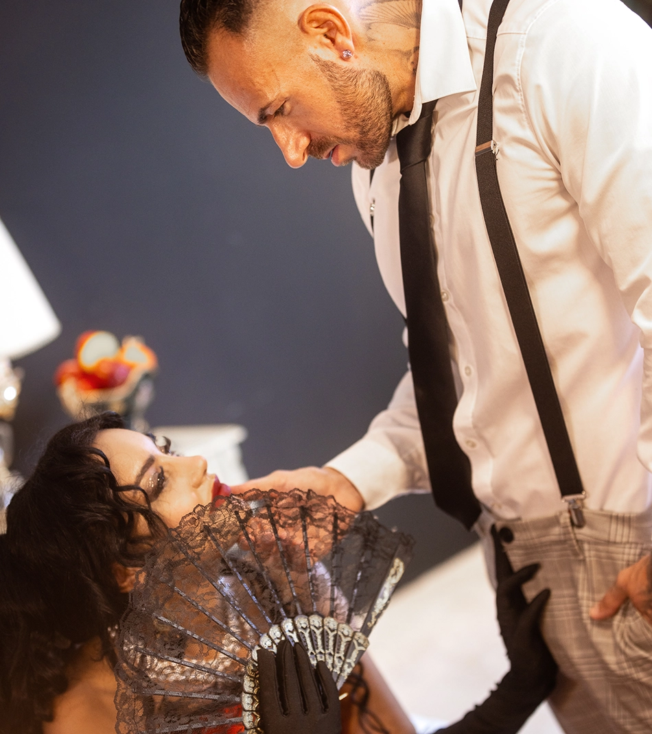 Snake Dave mit Hosenträgern beugt sich über Tänzerin mit Spitzenfächer – Burlesque-Shooting