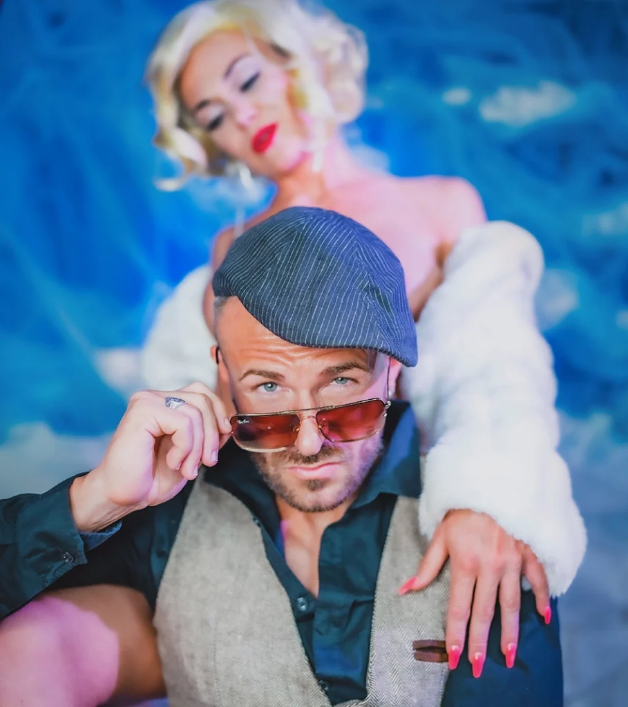 Snake Dave mit Schiebermütze und Sonnenbrille vor Pin-up-Girl im Marilyn-Monroe-Stil