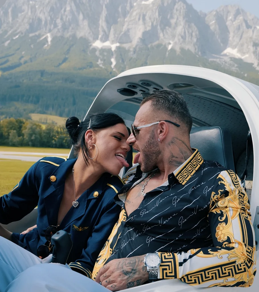 Snake Dave und Stewardess in romantischer Pose im Cockpit vor Bergpanorama